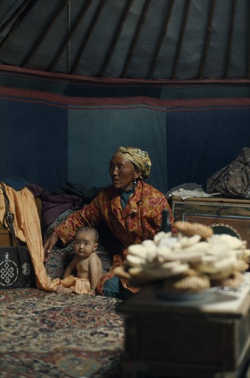 MONGOLIA, People, Khalkha winter sheep camp  ger yurt interior with grandmother looking after daughter's baby  traditional design wooden boxes for carrying all family posessions when moving from one area of the negdel to another e.g. for pasturing animals. Ger East Asia Asian Babies Female Women Girl Lady Kids Mongol Uls Mongolian