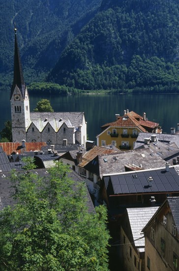 AUSTRIA, Oberosterreich, Hallstatt, "View over tiled village rooftops, hotel and church with Hallstattersee Lake and steep mountain backdrop."
