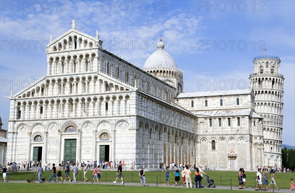 ITALY, Tuscany, Pisa, The Campo dei Miracoli Field of Miracles. Tourists walking past the 12th Century lombard-style facade of the Cathedral or Duomo with the 14th Century Leaning Tower beyond all within the UNESCO World Heritage site