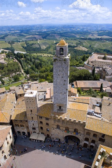 ITALY, Tuscany, San Gimignano, People in the Piazza del Duomo with the town's oldest tower of the Palazzo Vecchio Podesta built in 1239 with the farmland east of the town beyond