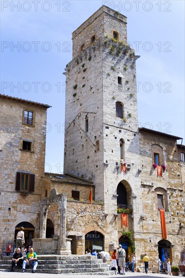 ITALY, Tuscany, San Gimignano, People gathering around the well in the Piazza della Cisterna with one of the town's medieval towers beyond above shops