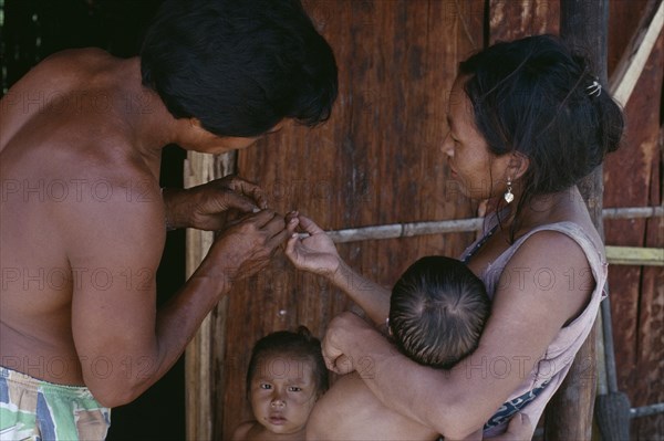 COLOMBIA, North West Amazon, Tukano Indigenous People, Makuna family.  Venancio removing thorn from his wife's finger with two young children partly seen. Tukano  Makuna Indian North Western Amazonia American Colombian Columbia Hispanic Indegent Kids Latin America Latino South America Tukano