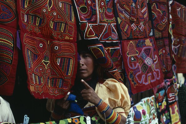 PANAMA, San Blas Islands, Kuna Indians, Kuna Indian woman looking out from between brightly coloured applique sewn molas for sale to tourist visitors.  Cuna Caribbean American Central America Colored Female Women Girl Lady Hispanic Latin America Latino Panamanian West Indies