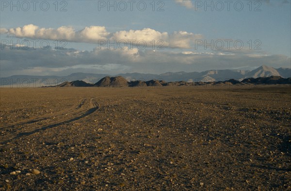 MONGOLIA, Gobi Desert, Summer landscape on the edge of the Gobi desert with vehicle tracks through expanse of barren stony ground and distant Altai mountains. East Asia Asian Mongol Uls Mongolian Scenic