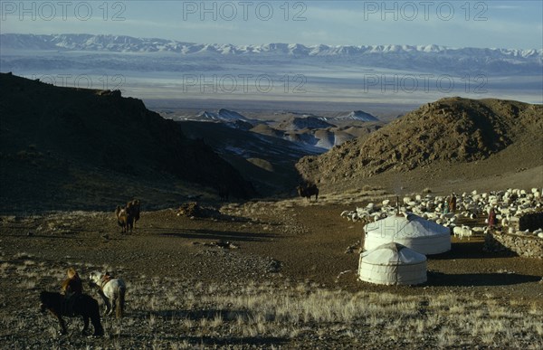MONGOLIA, Gobi Desert, Khalkha winter sheep camp with shepherd family homes  gers yurts   flock of sheep  hobbled horses and bactrian camels on hillside overlooking snow-covered mountain landscape with Altai mountains in distance.Khalkha East Asia Asian Equestrian Mongol Uls Mongolian Scenic