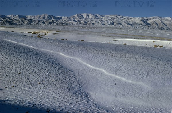 MONGOLIA, Gobi Desert, Biger Negdel, Mid-winter with snow-covered desert pastures. Onvoy of trucks brings fodder to outlying negdel collective. Altai mountains in background. East Asia Asian Mongol Uls Mongolian Scenic
