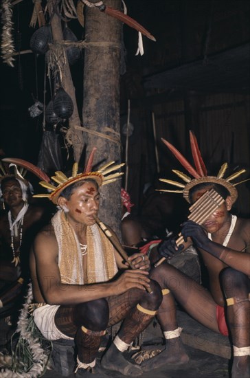 COLOMBIA, North West Amazon, Tukano Indigenous People, "Two Barasana musicians, one with flute the other with panpipes, rest after interminable dancing  both wearing cumare fibre garters and crowns of macaw and toucan feathers.  Tukano sedentary Indian tribe North Western Amazonia  American Colombian Columbia Hispanic Indegent Latin America Latino Religion South America Tukano Religious "