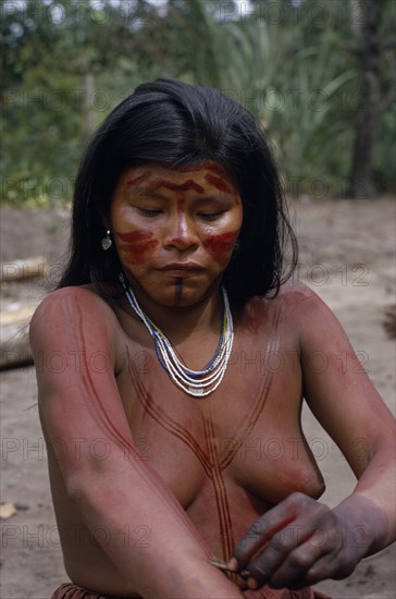 COLOMBIA, North West Amazon, Tukano Indigenous People, Young Barasana mother using cumare fibre bound twigs to apply red Achiote fruit  line pattern to upper body and arms.  Hands already coloured dark purple with we leaf dye to wrists.  Wearing white yellow and blue traded glass bead necklaces and silver earrings Tukano sedentary Indian tribe North Western Amazonia body decoration American Colombian Colored Columbia Female Women Girl Lady Hispanic Indegent Latin America Latino South America Tukano