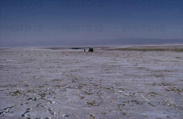 MONGOLIA, Gobi Desert, Mid-winter on the edge of the Gobi with a distant Russian Gaz jeep and lone figure walking in barren frozen landscape