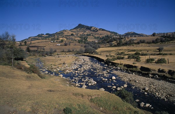 MEXICO, Michoacan State, El Rosario Butterfly Santuary, View across farmland and stream toward the butterfly sanctuary.