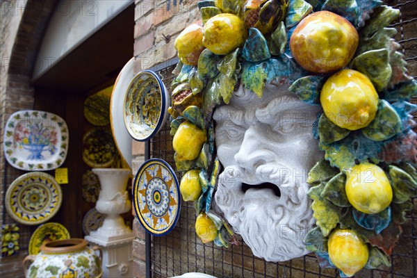 ITALY, Tuscany, San Gimignano, Outdoor shop display of ceramics with colourful plates and the face of a bearded man with fruit and vines in his hair