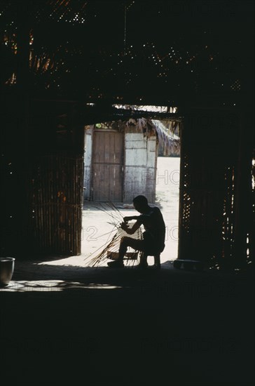 COLOMBIA, North West Amazon, Tukano Indigenous People, Makuna head man Ignacio making cane basket silhouetted at entrance to maloca or communal home. Tukano  Makuna Indian North Western Amazonia moloka American Colombian Columbia Hispanic Indegent Latin America Latino Male Men Guy South America Tukano