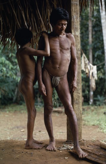 COLOMBIA, North West Amazon, Vaupes, Middle aged Maku nomad standing with his son beside frame of thatched home at base village.  indigenous tribe indian nomadic American Colombian Columbia Hispanic Indegent Kids Latin America Latino Male Men Guy South America Vaupes Male Man Guy Vaupes