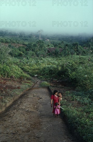 COLOMBIA, North West Amazon, Tukano Indigenous People, Makuna mother carrying baby and with young daughter in front of her walking between malocas along unmade road through cleared and cultivated rainforest. Tukano  Makuna Indian North Western Amazonia family American Babies Colombian Columbia Hispanic Indegent Kids Latin America Latino Mum Scenic South America Tukano
