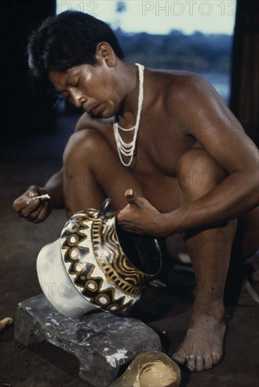 COLOMBIA, North West Amazon, Tukano Indigenous People, "Barasana tribesman painting white,yellow clay & black charcoal design onto yaje pot used to hold hallucinogenic yaje juice from vine species Banisteriopsis drunk during shamanic and religious ceremonies Tukano sedentary Indian tribe North Western Amazonia ayahuasca American Colombian Columbia Hispanic Indegent Latin America Latino Religion South America Tukano One individual Solo Lone Solitary "