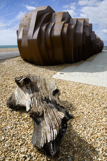 ENGLAND, West Sussex, Littlehampton, The rusted metal structure of the fish and seafood restaurant the East Beach Cafe designed by Thomas Heatherwick on the promenade with driftwood on the pebble beach in the foreground