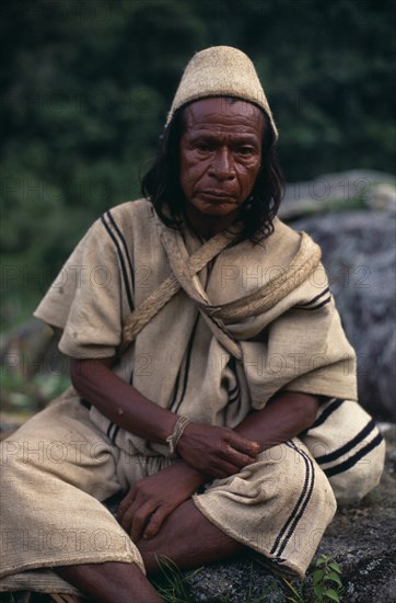 COLOMBIA, Sierra Nevada de Santa Marta, Ika, Portrait of Ika mama priest Juan de Jose wearing traditional cactus woven cactus fibre helmet and woven wool&cotton manta cloak and trousers. Fine spun cotton amulets on wrist to protect and ward off evil. Arhuaco Aruaco indigenous tribe American Colombian Colombia Hispanic Indegent Latin America Latino Religion South America  Arhuaco Aruaco indigenous tribe American Colombian Columbia Hispanic Indegent Latin America Latino Religion South America One individual Solo Lone Solitary Religious 1 Classic Classical Fiber Historical Older Single unitary