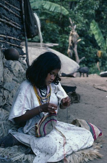 COLOMBIA, Sierra Nevada de Santa Marta, Ika, Ika girl outside her home in the Sierra sewing traditional woollen mochila shoulder bag. Wears traditional woven wool&cotton manta cloak and a necklace of many strings of glass beads - a sign of wealth Arhuaco Aruaco indigenous tribe American Classic Classical Colombian Colombia Hispanic Historical Indegent Kids Latin America Latino Older South America  Arhuaco Aruaco indigenous tribe American Classic Classical Colombian Columbia Hispanic Historical Indegent Kids Latin America Latino Older South America History One individual Solo Lone Solitary 1 Single unitary