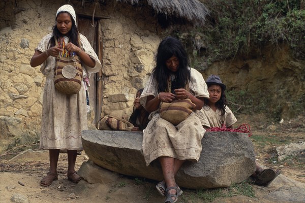 COLOMBIA, Sierra Nevada de Santa Marta, Ika, Ika women outside mud wattle thatched home sewing traditional woollen mochilas shoulder bags used by men and women for carrying personal belongings. Arhuaco Aruaco indigenous tribe American Classic Classical Colombian Colombia Female Woman Girl Lady Hispanic Historical Indegent Latin America Latino Older South America  Arhuaco Aruaco indigenous tribe American Classic Classical Colombian Columbia Female Woman Girl Lady Hispanic Historical Indegent Latin America Latino Older South America Female Women Girl Lady History Male Man Guy