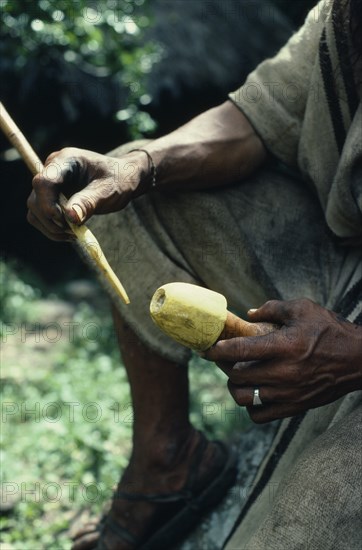 COLOMBIA, Sierra Nevada de Santa Marta, Ika, Cropped detail of Ika man holding a poporo small gourd containing finely powdered lime.Ika men can spend hours rubbing their gourds with their palitos small sticks  in ceremonies in conversation or in thought.The process has a deep socio-religious-sexual significance.The stick is the male penis  the gourd the female vagina and the rubbing the sexual act.The lime acts as a catalyst to extract cocaine alkaloid from wad of chewed leaves constantly held in the cheek. Arhuaco Aruaco indigenous tribe American Colombian Colombia Hispanic Indegent Latin America Latino Male Men Guy South America  Arhuaco Aruaco indigenous tribe American Colombian Columbia Hispanic Indegent Latin America Latino Male Men Guy South America Male Man Guy One individual Solo Lone Solitary 1 Perform Single unitary