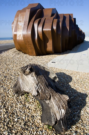 ENGLAND, West Sussex, Littlehampton, The rusted metal structure of the fish and seafood restaurant the East Beach Cafe designed by Thomas Heatherwick on the promenade with driftwood on the pebble beach in the foreground