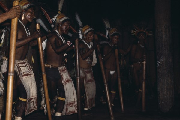 COLOMBIA, North West Amazon, Tukano Indigenous People, "Barasana stave dance hollow yarumo wood staves rhythmically pounded on ground Line of male dancers wear painted barkcloth aprons and ceremonial royal crane,toucan & macaw feather head-dresses, their faces painted with red Achiote fruit dye. Tukano sedentary Indian tribe North Western Amazonia American Colombian Columbia Hispanic Indegent Latin America Latino Performance South America Tukano "
