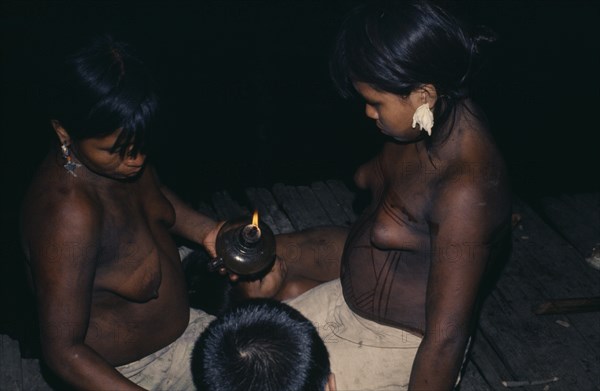 COLOMBIA, Choco, Embera Indigenous People, Young Embera daughters of the household painting their bodies with black dye extracted from the indedible Jagua fruit in preparation for curing ceremony - their mother has fever  Pacific coastal region tribe body decoration American Colombian Colombia Female Woman Girl Lady Hispanic Indegent Latin America Latino South America  Pacific coastal region tribe body decoration American Colombian Columbia Female Woman Girl Lady Hispanic Indegent Latin America Latino South America Female Women Girl Lady Immature Mum Young Unripe Unripened Green