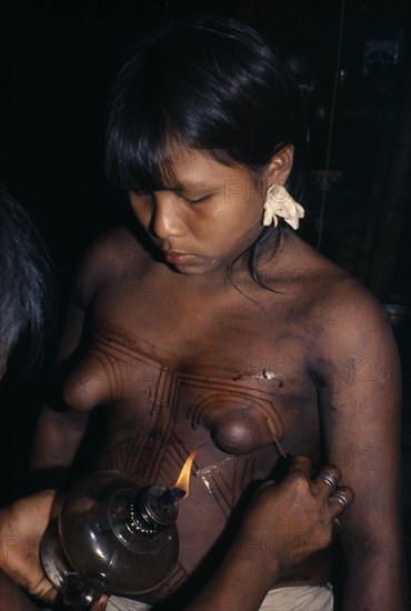 COLOMBIA, Choco, Embera Indigenous People, Young Embera daughters with sweet-smelling lilies in their ears  paint their bodies with black dye extracted from the indedible Jagua fruit in preparation for their mother's curing ceremony. Pacific coastal region tribe body decoration American Colombian Colombia Female Woman Girl Lady Hispanic Indegent Latin America Latino South America  Pacific coastal region tribe body decoration American Colombian Columbia Female Woman Girl Lady Hispanic Indegent Latin America Latino South America Female Women Girl Lady Immature Young Unripe Unripened Green