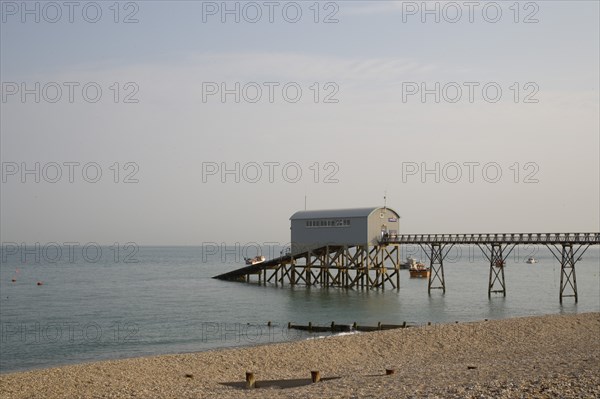 ENGLAND, West Sussex, Selsey, Royal National Lifeboat Institution. View across shingle beach towards a pier with RNLI station