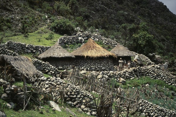 COLOMBIA, Sierra Nevada de Santa Marta, Ika Indigenous People, Ika family settlement in high Sierra  with three circular conical thatched huts and stone wall terraces set into hillside. Ika father and children standing outside central hut. Arhuaco Aruaco indigenous tribe American Colombian Colombia Hispanic Kids Latin America Latino Male Men Guy Scenic South America  Arhuaco Aruaco indigenous tribe American Colombian Columbia Hispanic Kids Latin America Latino Male Men Guy Scenic South America 3 Indegent Male Man Guy Dad
