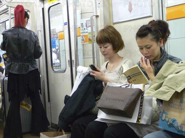 JAPAN, Honshu, Tokyo, "Ginza - three women on a subway train, right side young woman, shopping bags including Louis Vuitton, woman in the middle using cell phone text message, standing woman (left) with bright red pony tail, dressed in black"