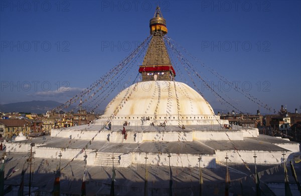 20086659 NEPAL Kathmandu Valley Bodhnath People circumambulate giant central stupa hung with prayer flags and painted with eyes of Buddha. Town spread out beyond.