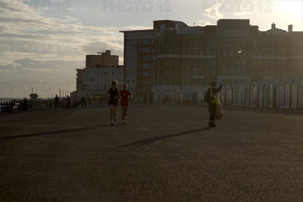 ENGLAND, East Sussex, Brighton, Silhoetted joggers on the seafront at Hove Lawns.