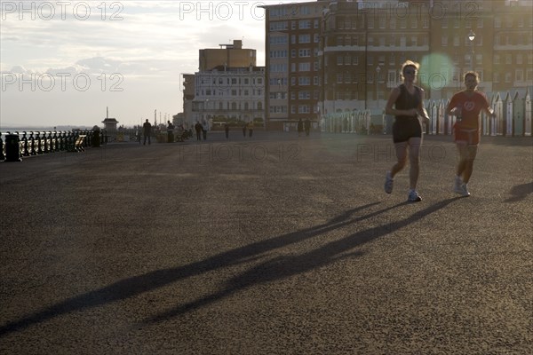 ENGLAND, East Sussex, Brighton, Silhoetted joggers on the seafront at Hove Lawns.