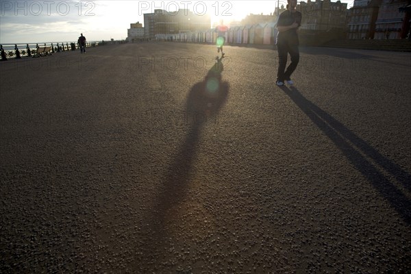 ENGLAND, East Sussex, Brighton, Silhoetted joggers on the seafront at Hove Lawns.