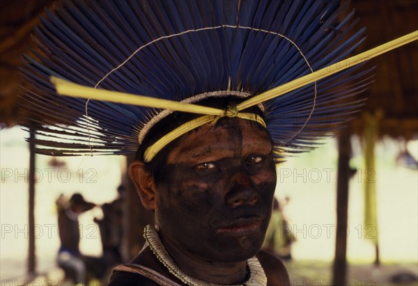 BRAZIL, Mato Grosso, Indigenous Park of the Xingu, Portrait of Panara male elder wearing ceremonial crown made from blue parrot feathers  face painted black from eyes to neck.Relocated in Xingu National Park by Villas Boas brothers Formally known as Kreen-Akrore  Krenhakarore  Krenakore  Krenakarore  Amazon American Brasil Brazilian Indegent Kreen Akrore Latin America Latino South America  Formally known as Kreen-Akrore  Krenhakarore  Krenakore  Krenakarore  Amazon American Brasil Brazilian Indegent Kreen Akore Latin America Latino South America One individual Solo Lone Solitary 1 Single unitary