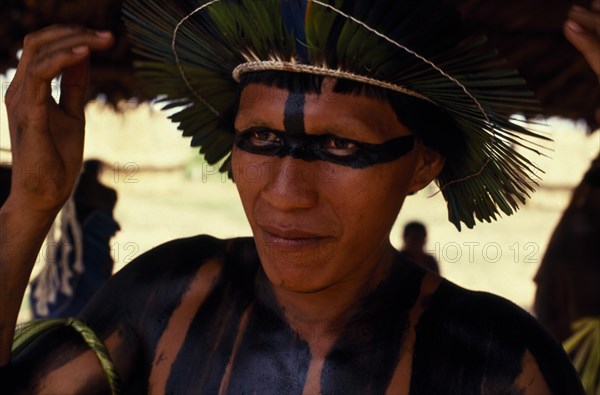 BRAZIL, Mato Grosso, Indigenous Park of the Xingu, Head and shoulders portrait of young  male Panara leader wearing crown made from green parrot feathers and black face and body paint. Formally known as Kreen-Akrore  Krenhakarore  Krenakore  Krenakarore  Amazon American Brasil Brazilian Indegent Kreen Akrore Latin America Latino South America  Formally known as Kreen-Akrore  Krenhakarore  Krenakore  Krenakarore  Amazon American Brasil Brazilian Indegent Kreen Akrore Latin America Latino South America Immature One individual Solo Lone Solitary 1 Single unitary Young Unripe Unripened Green