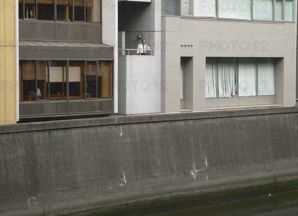 JAPAN, Honshu, Tokyo, "Nihonbashi - at lunchtime, a ""salariman"" office worker in white shirt and time takes break, smoking cigarette, looking in to Nihonbashi river, bleak urban landscape"