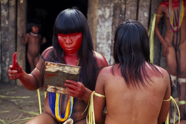 BRAZIL, Mato Grosso, Indigenous Park of the Xingu, Young Panara women applying red karajuru face and body paint in preparation for dance.   Formally known as Kreen-Akrore  Krenhakarore  Krenakore  Krenakarore  Amazon American Brasil Brazilian Female Woman Girl Lady Indegent Kreen Akore Latin America Latino South America Female Women Girl Lady Immature