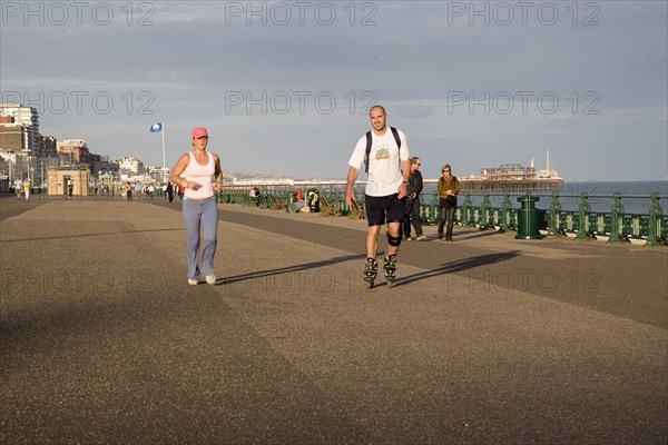 ENGLAND, East Sussex, Brighton, Woman jogging with man rollerblading on the seafront promenade.