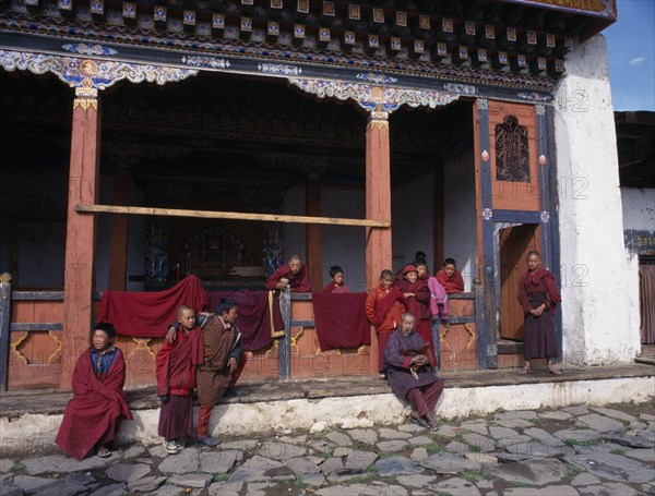 BHUTAN, Gantey Gompa, Group of young novice monks with older man holding cockerel gathered on step outside traditionally painted gompa or monastery.