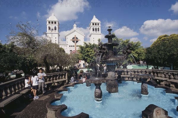 EL SALVADOR, Juayua, Temple del Senor de Juayua and Plaza.  Children beside fountain in foreground with white exterior facade of the Church of the Cristo Negro or Black Christ behind.
