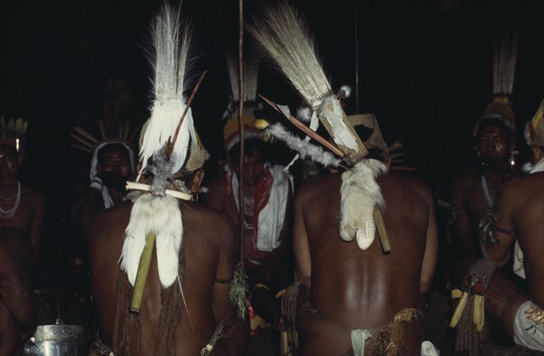 COLOMBIA, North West Amazon, Tukano Indigenous People, Rear view of two Barasana shamans wearing royal crane macaw and toucan head-dresses with monkey fur belts chanting to chief shaman Cristo in background  between traditional dances. Tucano sedentary Indian tribe North Western Amazonia American Classic Classical Colombian Columbia Hispanic Historical Indegent Latin America Latino Older Religion South America Tukano History Religious