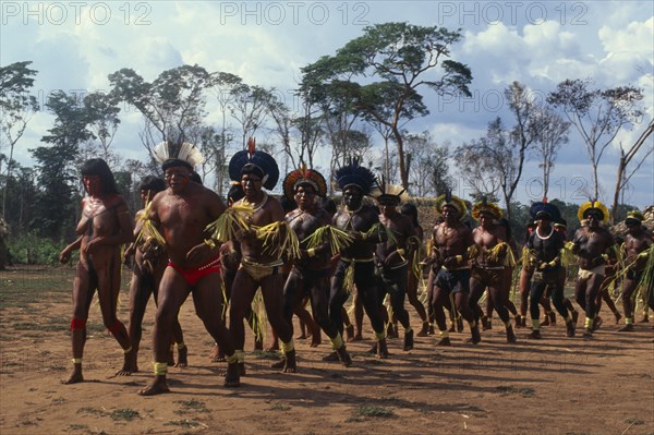 BRAZIL, Mato Grosso, Indigenous Park of the Xingu, Panar‡ men and women performing traditional dance around central area of relocated village in Xingu National Park.  Men wearing head-dresses or crowns of feathers and face and body paint. Formally known as Kreen-Akrore  Krenhakarore  Krenakore  Krenakarore  Amazon American Brasil Brazilian Classic Classical Female Woman Girl Lady Historical Indegent Kreen Akore Latin America Latino Male Man Guy Older Performance South America