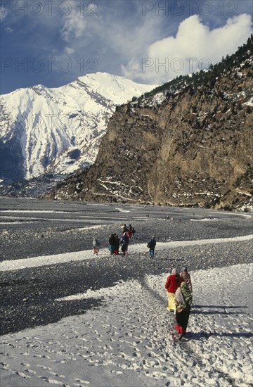 NEPAL, Annapurna Region, Khobang, Circuit Trek. Thakali villagers walking on the snow covered trail between Tukuche and Khobang