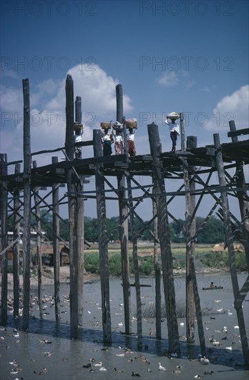 THAILAND, North, Bridges, Women carrying baskets on their heads crossing high wooden bridge across river and ducks.