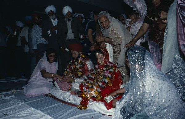 ENGLAND, Religion, Sikhism, Bride and groom receiving gifts of money from guests during wedding ceremony.