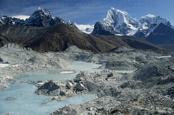 NEPAL, Everest Trek, Near Gokyo, Trekkers crossing an ice lake on the Ngozumpa Glacier with mountains Cholatse on the left and Tawachee on the right in the background.