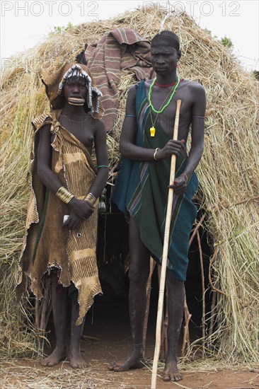 ETHIOPIA, South Omo Valley, Mursi Tribe, Couple standing outside their hut
