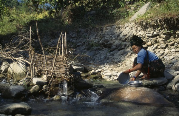 NEPAL, Manaslu Circuit Trek, Arughat, Woman washing pots beside a fish trap in a tributary river near Arughat Village